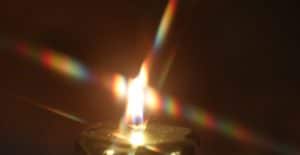 Leuchtende Kerzenflamme mit farbigen Lichtbrechungen im Dunkeln – Sinnbild für geistige Knotenpunkte und die Kräfte des Guten im schamanischen Seminar.
