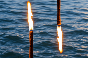Spirituelles Heilen - Modul 6. Zwei brennende Fackeln vor bewegtem Wasser, eine Flamme nach oben, die andere nach unten gerichtet – Sinnbild für den Heilerweg und den Schamanenweg.
